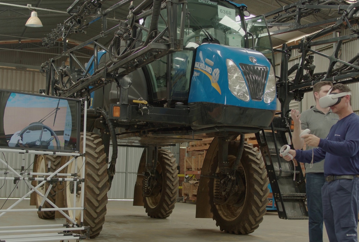 A CNH employee conducts operator training for a New Holland sprayer using a virtual reality headset and controls