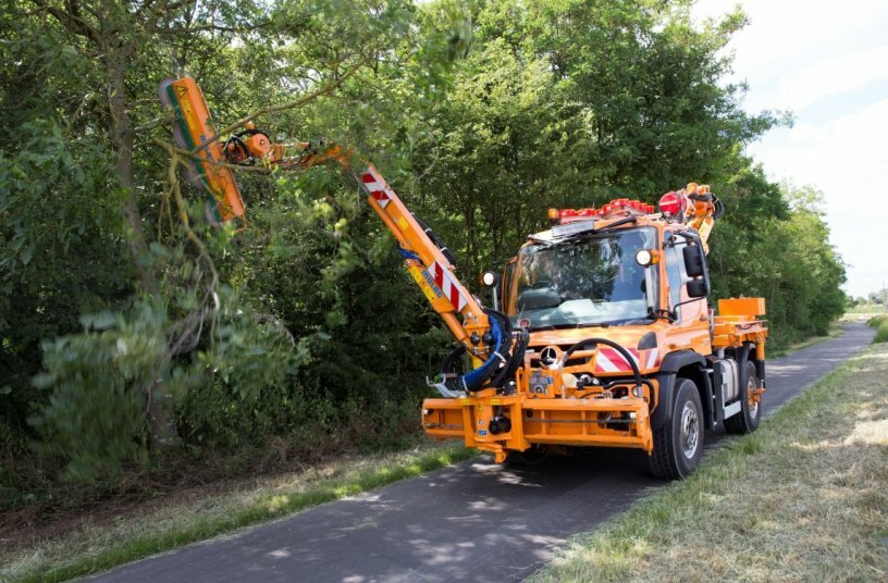 Unimog implement carrier with front mower, hedge trimmer, and spreader