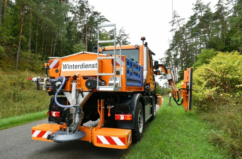 Unimog implement carrier with front mower, hedge trimmer, and spreader