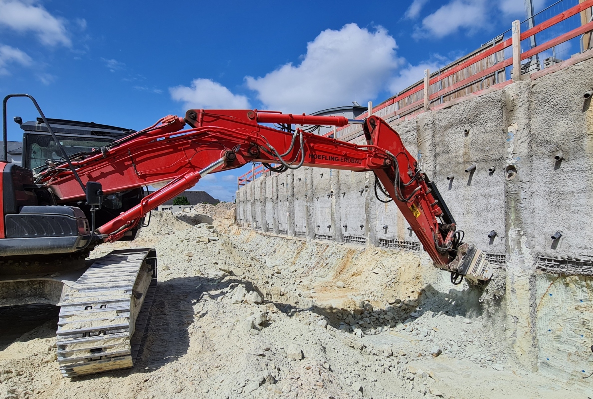 Using a 25-tonne short-tail excavator and a KR 120 rotary drum cutter from KEMROC, the contractor Höfling profiles the shoring wall before lining with steel mesh and shotcrete on the Königsteiner Höfe construction site.