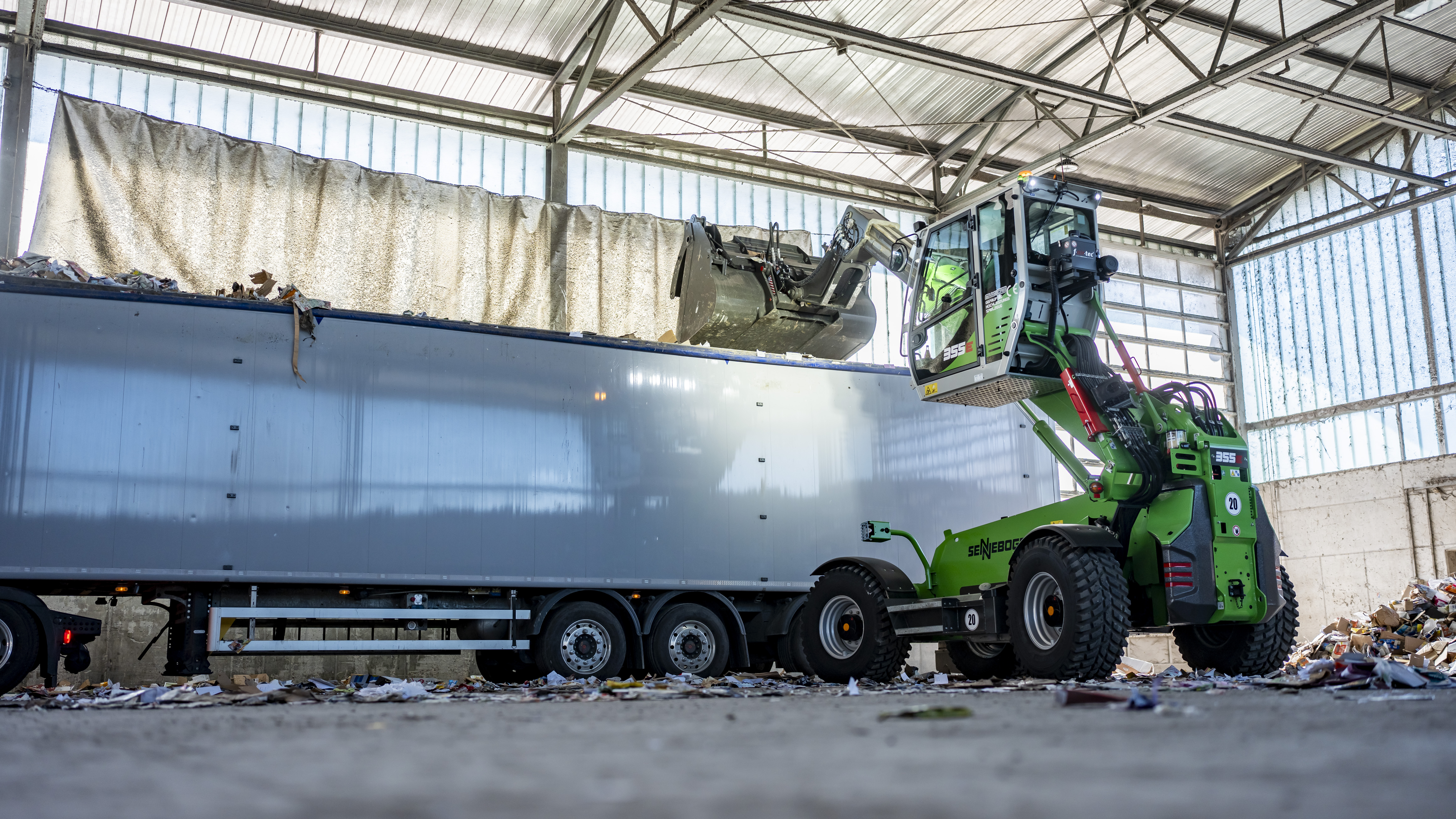 The SENNEBOGEN 340 G effortlessly loads waste into a truck with its telescopic arm.