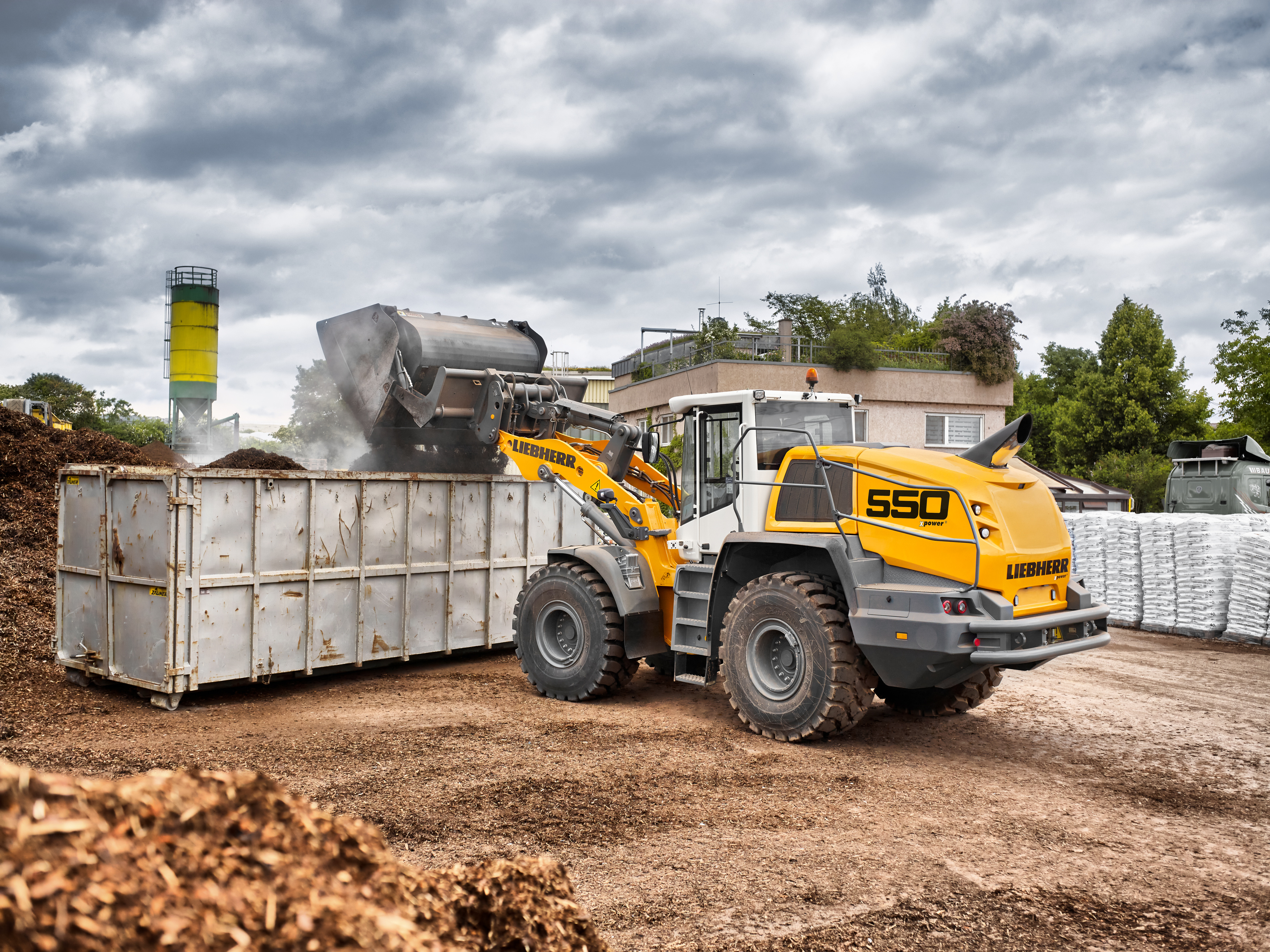 An L 550 XPower® with industrial kinematics and high dump bucket loading a container.