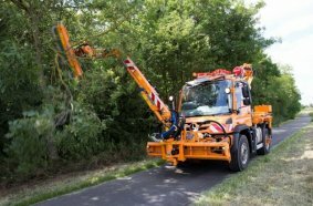 Unimog implement carrier with front mower, hedge trimmer, and spreader