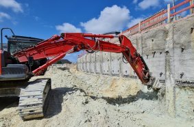 Using a 25-tonne short-tail excavator and a KR 120 rotary drum cutter from KEMROC, the contractor Höfling profiles the shoring wall before lining with steel mesh and shotcrete on the Königsteiner Höfe construction site.
