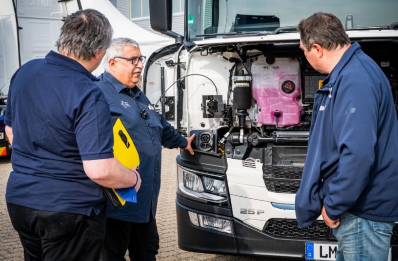 Fahrlehrer Frank Hartmann erklärt den Bona-Werksfahrern Enrico Wachsmann (re.) und Gunther Heinritz (li.), wo und wie der vollelektrische Scania 25 P geladen wird.<br>BILDQUELLE: Scania Deutschland Österreich