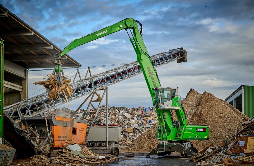 The green all-rounder feeds waste wood to a shredder at the Wurzer Umwelt site in Eitting.<br>IMAGE SOURCE: SENNEBOGEN
