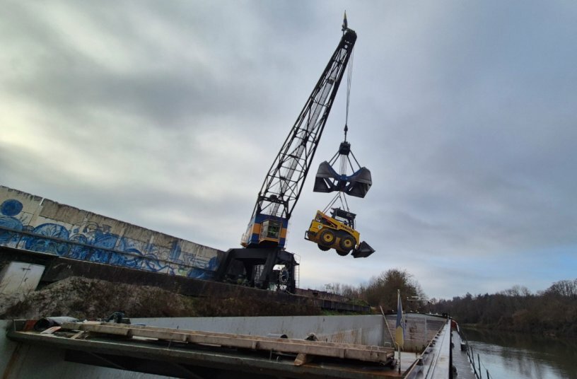 Damit der Kompaktlader reibungslos auf dem Schiff operieren kann, wurde er von Krieger individuell angepasst: Unter anderem erhielt er einen Heckanfahrschutz für zusätzliche Sicherheit und wurde für die Kranverladung vorbereitet – denn bei jedem Ladeort wird er per Hafendrehkran ein- und ausgeschifft.<br>BILDQUELLE: KUHN Baumaschinen Deutschland GmbH