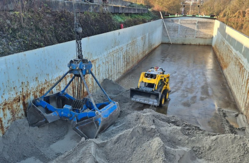 Im Laderaum der Heiner Krieger übernimmt der kompakte Komatsu SK715-8 eine zentrale Aufgabe: Er schiebt Sand und Kies so zusammen, dass das Material effizient vom eigenen Seilbagger entnommen und entladen werden kann.<br>BILDQUELLE: KUHN Baumaschinen Deutschland GmbH