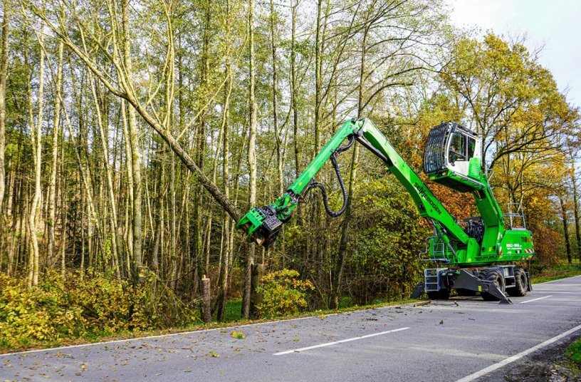 The SENNEBOGEN 718 E works with a grapple saw during tree care along a wooded road.<br>IMAGE SOURCE: SENNEBOGEN Maschinenfabrik GmbH
