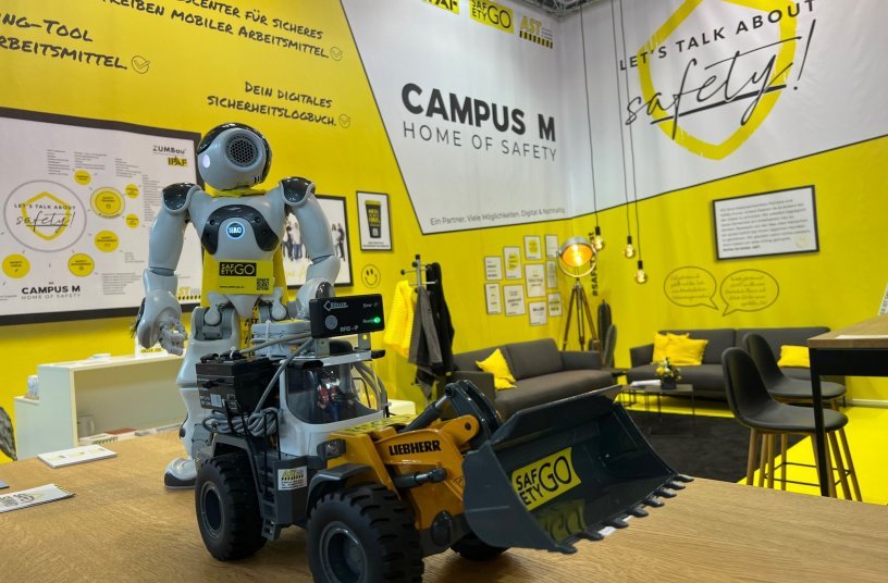 Messeauftritt mit Roboter Nao. Die SafetyGO GmbH & Co. KG und die AST Arbeitssicherheit und Technik GmbH präsentierten auf der bauma 2022 auf einem in auffallend Gelb gehaltenen Stand gemeinsam digitale Angebote.<br>BILDQUELLE: AST GmbH