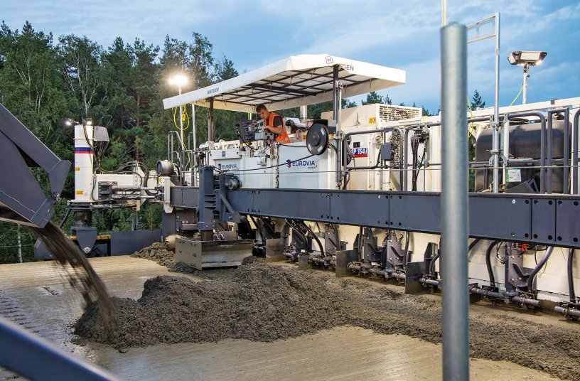 A belt conveyor is used to convey the top layer concrete over and across the first SP 154(i) (operating as a bottom layer paver) onto the freshly paved bottom layer concrete directly in front of the second SP 154(i) (operating as a top layer paver) for further processing. <br>Image source: Wirtgen GmbH