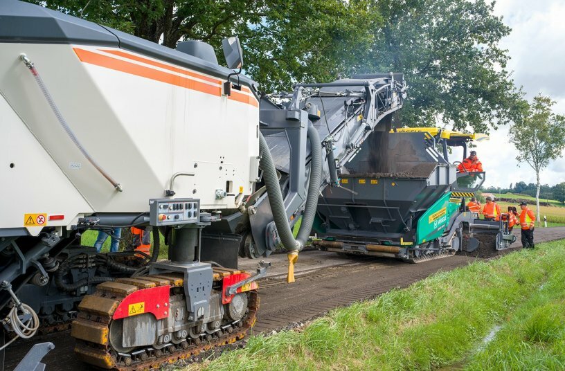   The material is transferred directly to the material hopper of the Vögele SUPER 2100-5i paver and laid down as the train advances.<br>IMAGE SOURCE: WIRTGEN GROUP
