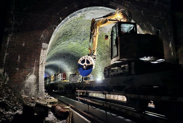 An 8-ton excavator with a KDS 30 diamond saw enters the Elleringhauser Tunnel on a platform truck. The task is to cut concrete cable ducts at the bottom of the tunnel walls.