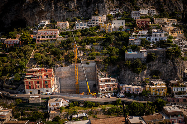 A Grove GMK4100L-1 all-terrain crane is assembling the Potain MDT 189 tower crane to help construct a multi-story parking lot and elevator into the rockface